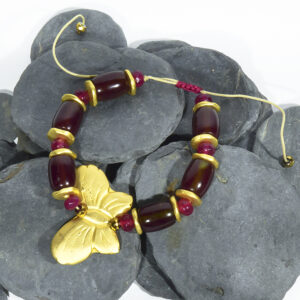 Pulsera artesanal con mariposa en oro mate y ágatas barril bicolor con granates facetados.
